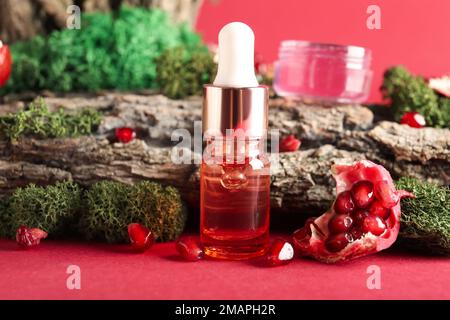 Flacone contagocce cosmetico con muschio verde, melograno e corteccia d'albero su sfondo rosso, primo piano Foto Stock