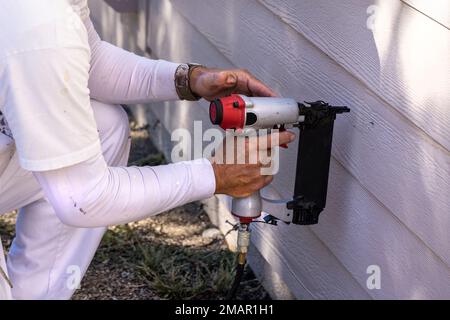 Pittore usando una pistola per unghie per riparare il lato della casa prima di iniziare il lavoro di vernice Foto Stock