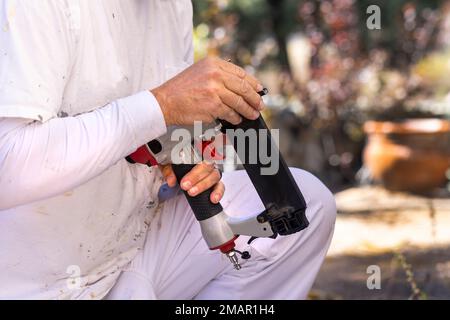 Pittore usando una pistola per unghie per riparare il lato della casa prima di iniziare il lavoro di vernice Foto Stock