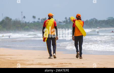 Due bagnini in servizio presso la spiaggia tropicale, entrambi trasportano tubi di salvataggio sulle spalle e camminano sulla spiaggia di sabbia tropicale a Weligama. Foto Stock