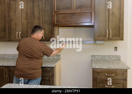 Lavoratore appeso livello in preparazione per il livellamento di nuovo mobile armadio da cucina set che sarà installato Foto Stock