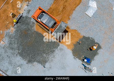 Sulla benna per cantiere collegata, viene utilizzato un escavatore per livellare la ghiaia prima di versare il calcestruzzo per la fondazione di edifici Foto Stock