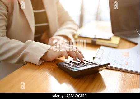 Professionista asiatico contabile femminile utilizzando la calcolatrice, lavorando su vendite e conti rapporto in ufficio. immagine della mano ritagliata e ravvicinata Foto Stock