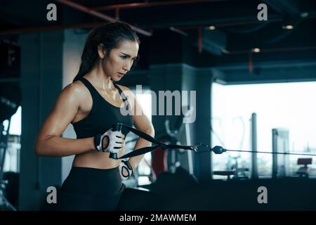 Donna sportiva che si esercita sulla multistazione in palestra per i muscoli delle braccia e delle spalle. Fitness in palestra. Foto Stock