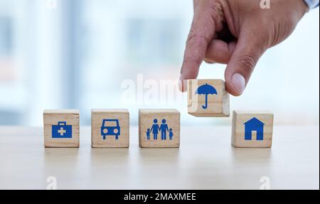 Mani, blocchi di legno e la costruzione sul tavolo per le basi essenziali o lo stile di vita sicuro della fondazione. Mano di persona che mette piccolo blocco di legno, oggetto o. Foto Stock