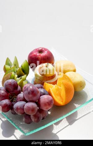 Frutta fresca in piatto su tavolo bianco. Frutti accettabili per il diabete. Kiwis, uva, arancia, mele, pere, dieta sana e dieta a basso contenuto calorico Foto Stock