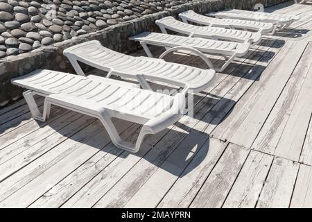 In una giornata di sole, i lettini in plastica bianca sono disponibili su una terrazza in legno Foto Stock