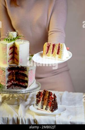 la ragazza taglia e serve un pezzo di torta. festa di nozze torta a due livelli decorata con fiori freschi Foto Stock
