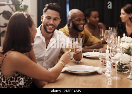 Im grato abbiamo incontrato. Una giovane coppia felice seduta con gli amici e brindisi con champagne durante una festa di Capodanno. Foto Stock