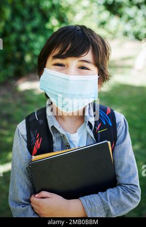 Torna a scuola oggi. un ragazzino che indossa uno zaino mentre trasporta libri in natura. Foto Stock