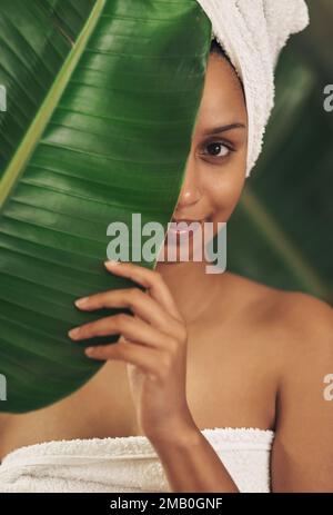 Mantengalo naturale in modo da non dovete nascondersi dietro il make-up. una bella giovane donna che indossa un asciugamano intorno alla testa mentre si posa dietro una foglia verde. Foto Stock