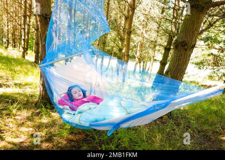 Bambina che si rilassa in una giornata di sole in amaca con zanzariera nella foresta. Foto Stock