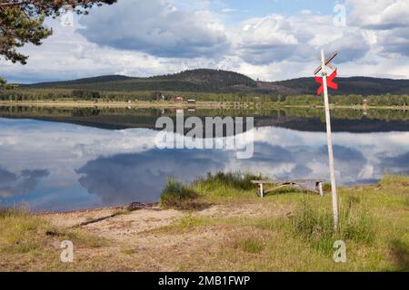 Edifici lungo il fiume sul lato opposto. Prati, colline, e un fiume dolce su questo lato. Cartello rosso per motoslitta. Foto Stock