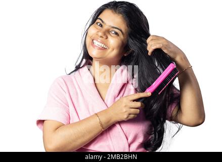 Una donna indiana abbastanza felice spazzolando i capelli indossando accappatoio su sfondo bianco Foto Stock