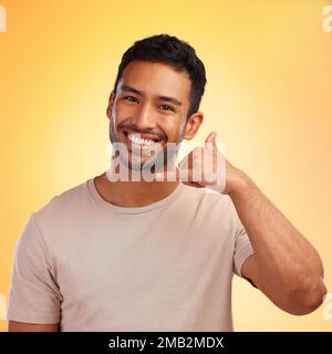 Ritratto, chiamami mani e uomo in studio isolato su uno sfondo giallo. Viso, moda e modello maschile felice con un gesto di mano fresco per shaka segno Foto Stock