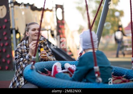 Un ragazzo, persona con sindrome di Down cammina nel parco con la madre, bolle di sapone Foto Stock