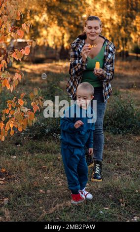 Un ragazzo, persona con sindrome di Down cammina nel parco con la madre, bolle di sapone Foto Stock