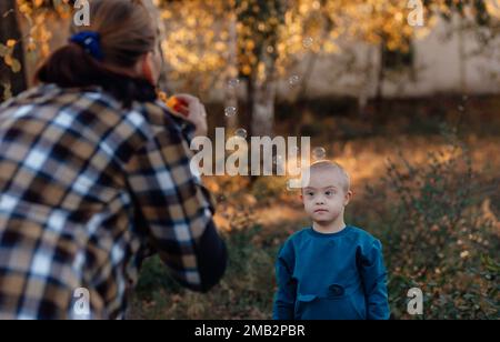 Un ragazzo, persona con sindrome di Down cammina nel parco con la madre, bolle di sapone Foto Stock