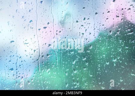 Gocce d'acqua scendono dal vetro. Sfondo sfocato astratto con luci bokeh. Condensa sulla finestra. Sfondo sfocato della strada della città in piovoso Foto Stock