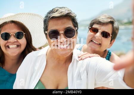 La vita è un'avventura meglio condivisa con gli amici. un gruppo maturo di amici in piedi e in posa per un selfie durante una giornata in spiaggia. Foto Stock