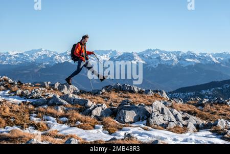 Alpinista che fa un grande passo, di fronte al panorama montano, sentiero escursionistico a Guffertstein, in background cresta principale delle Alpi con Foto Stock