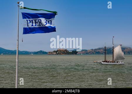 Bandiera del Molo 39 e storica barca a vela nella baia di San Francisco, l'isola di Alcatraz sul retro, San Francisco, California, Stati Uniti, Nord America Foto Stock