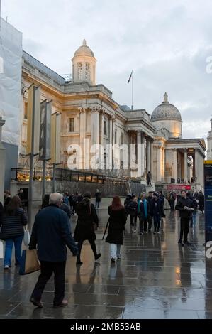 Persone che camminano sotto la pioggia presso la National Gallery illuminata di Trafalgar Square al tramonto a LONDRA, Inghilterra Foto Stock