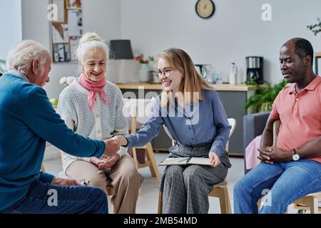 Giovane psicoterapeuta sorridente che saluta gli anziani durante la loro sessione Foto Stock