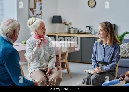 Giovane donna che ascolta gli anziani mentre si siedono sulle sedie durante la terapia in camera Foto Stock