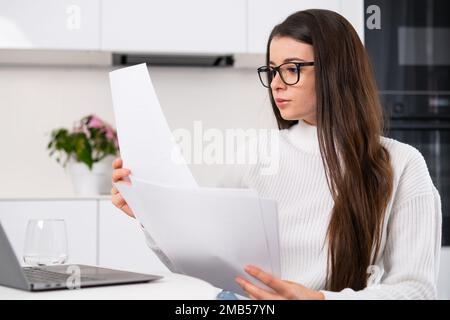 Allegra signora che tiene la carta utilizza un computer e funziona in remoto. Concetto di lavoro freelance a distanza. Foto Stock