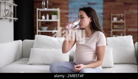 Donna incinta mano con un bicchiere di acqua e vitamina pillola Foto Stock