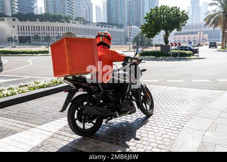 Un corriere di consegna del cibo sta guidando un ordine a casa di un cliente su un ciclomotore. cibo da asporto durante la quarantena. trasporto consegna pacchi a domicilio. m Foto Stock