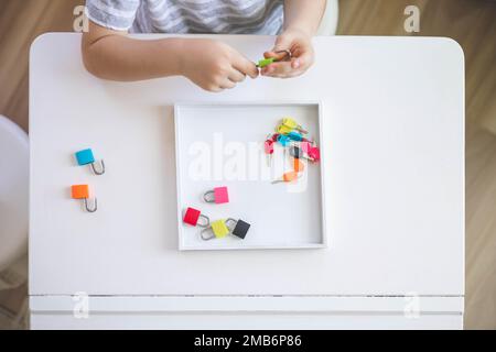 Il bambino lavora con materiale Montessori con serrature colorate. Raccoglie i tasti. Sviluppa le abilità motorie fini. Foto Stock