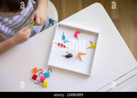 Il bambino lavora con materiale Montessori con serrature colorate. Raccoglie i tasti. Sviluppa le abilità motorie fini. Foto Stock