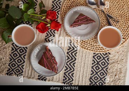 Colazione festiva con torte al cioccolato alla ciliegia, tazze da caffè, rose rosse e San Valentino, piatto estetico. Foto Stock