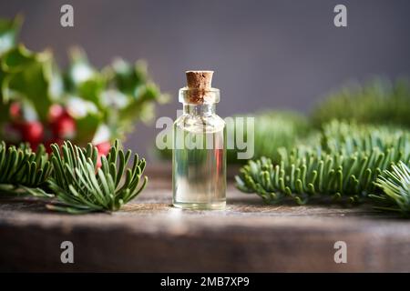 Bottiglia di olio essenziale con rami di abete e bacche agrifoglio sullo sfondo Foto Stock