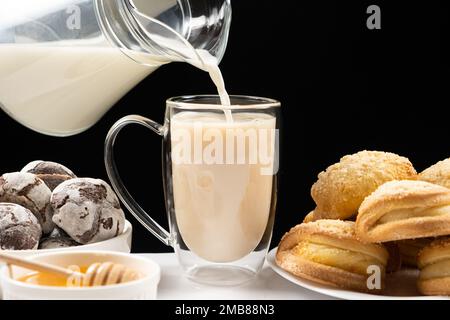 Preparazione del tè al latte - il latte di una brocca di vetro viene versato nel tè inglese nero. Foto Stock