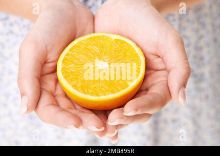 Ti offre un arancio. Immagine ritagliata di una mano donna che tiene mezzo arancione. Foto Stock
