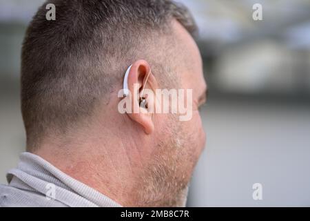 Vista posteriore di un uomo dai capelli grigi di mezza età duro dell'udito negli anni cinquanta o sessanta con un apparecchio acustico nell'orecchio Foto Stock