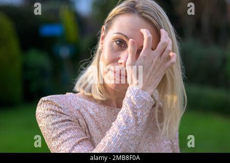 Bella bella donna bionda attraente nei suoi anni '40 in piedi nel giardino strozzato i suoi capelli Foto Stock