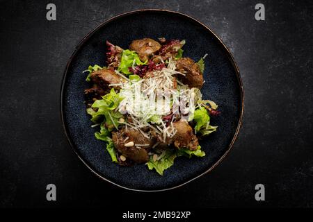 Insalata calda con fegato, formaggio e lattuga, su fondo scuro Foto Stock