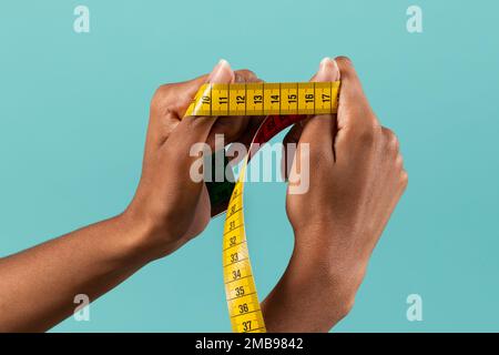 Crop anonimo afro-americano mani femminili dimostrando giallo metro nastro su sfondo turchese Foto Stock