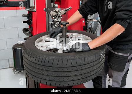 Angolo elevato di anonimo tecnico maschile in abiti e guanti casual girando le viti sul disco durante lo smontaggio del pneumatico durante il lavoro in garage Foto Stock