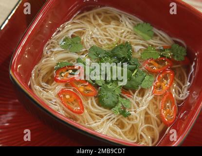 Brodo orientale servito con peperoncino, tagliatelle di riso e coriandolo a fette. Foto Stock