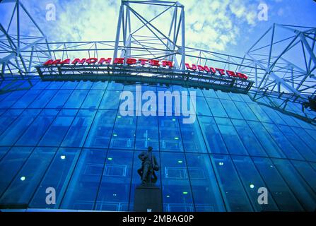 Old Trafford Football Stadium, Old Trafford, Trafford, 2003. Guardando verso la parete vetrata della tenda della tribuna est dello stadio di calcio Old Trafford, con la statua di bronzo di Sir Matt Busby di fronte. Foto Stock