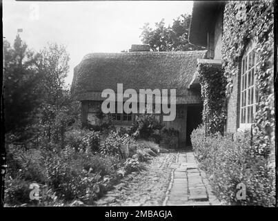 Wootton Rivers, Wiltshire, 1923. Il percorso e il giardino di un cottage con tetto di paglia a Wootton Rivers. Nell'indice negativo della collezione, il fotografo registra anche il 'semaforo di salvataggio a sinistra'. Nell'angolo in alto a sinistra della fotografia ci sono figure in un 'nido di corvo' con una bandiera. Foto Stock