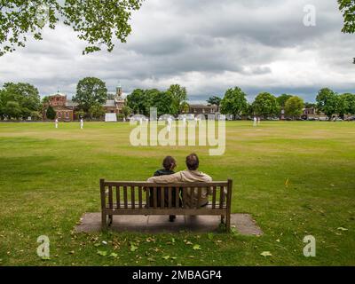 Kew Green, Kew, Richmond upon Thames, Greater London Authority, 2013. Due persone su una panchina sul Kew Green che guardano una partita di cricket giocata dal Kew Cricket Club. Cricket è stato giocato su Kew Green dagli anni '1730s. Il Kew Cricket Club è stato fondato nel 1882. Foto Stock