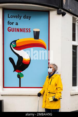 Blythe Hill Tavern, Stanstead Road, Forest Hill, Lewisham, Greater London Authority, 2022. Vista generale che mostra una donna in una maschera protettiva Covid-19 in piedi accanto a un poster pubblicitario Guinness nell'angolo sud-est della Blythe Hill Tavern. Foto Stock