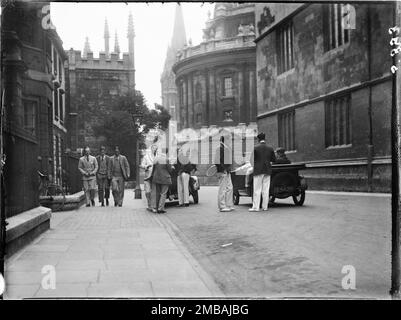 Hertford College, Oxford, Oxfordshire, 1928. Un gruppo di studenti maschi che indossano borse Oxford, in piedi accanto a due auto a motore su Catte Street fuori Hertford College. Foto Stock