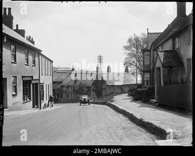 The Street, Charmouth, West Dorset, Dorset, 1925. Una vista della strada dall'Axminster Road End, guardando verso cottage dal tetto di paglia all'incrocio con l'Higher Sea Lane e mostrando un'auto a motore che sale sulla collina. Foto Stock